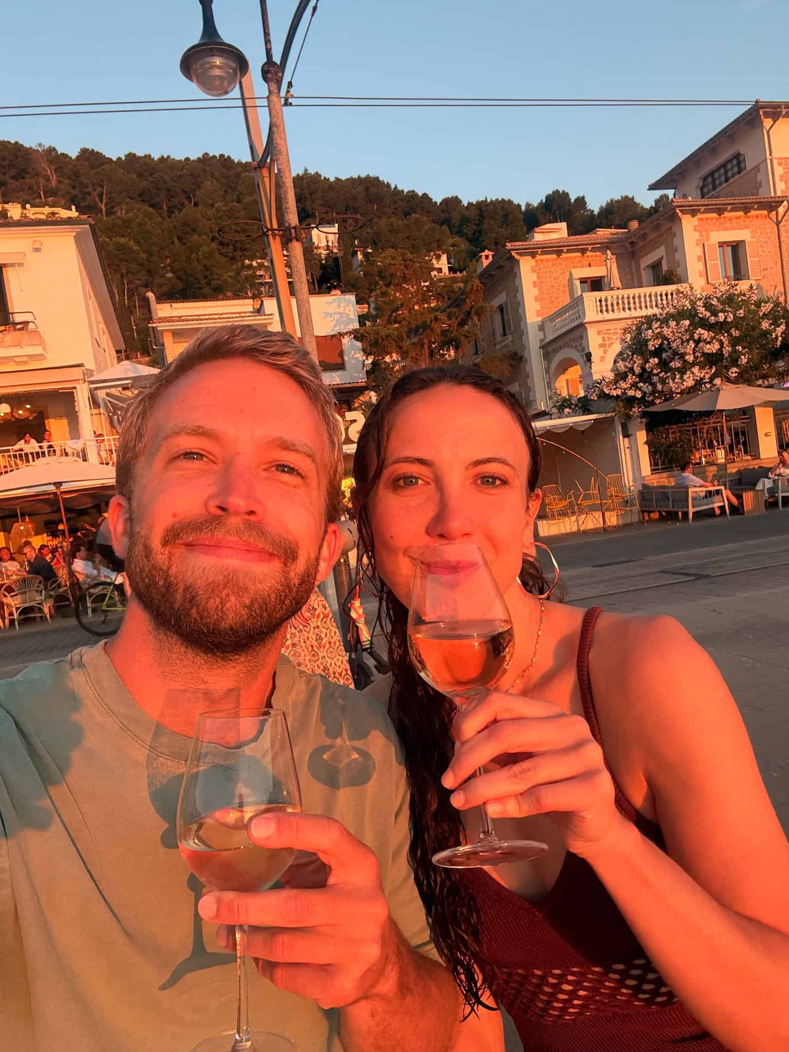 Couple toasting with wine glasses at golden hour on the Port de Soller waterfront