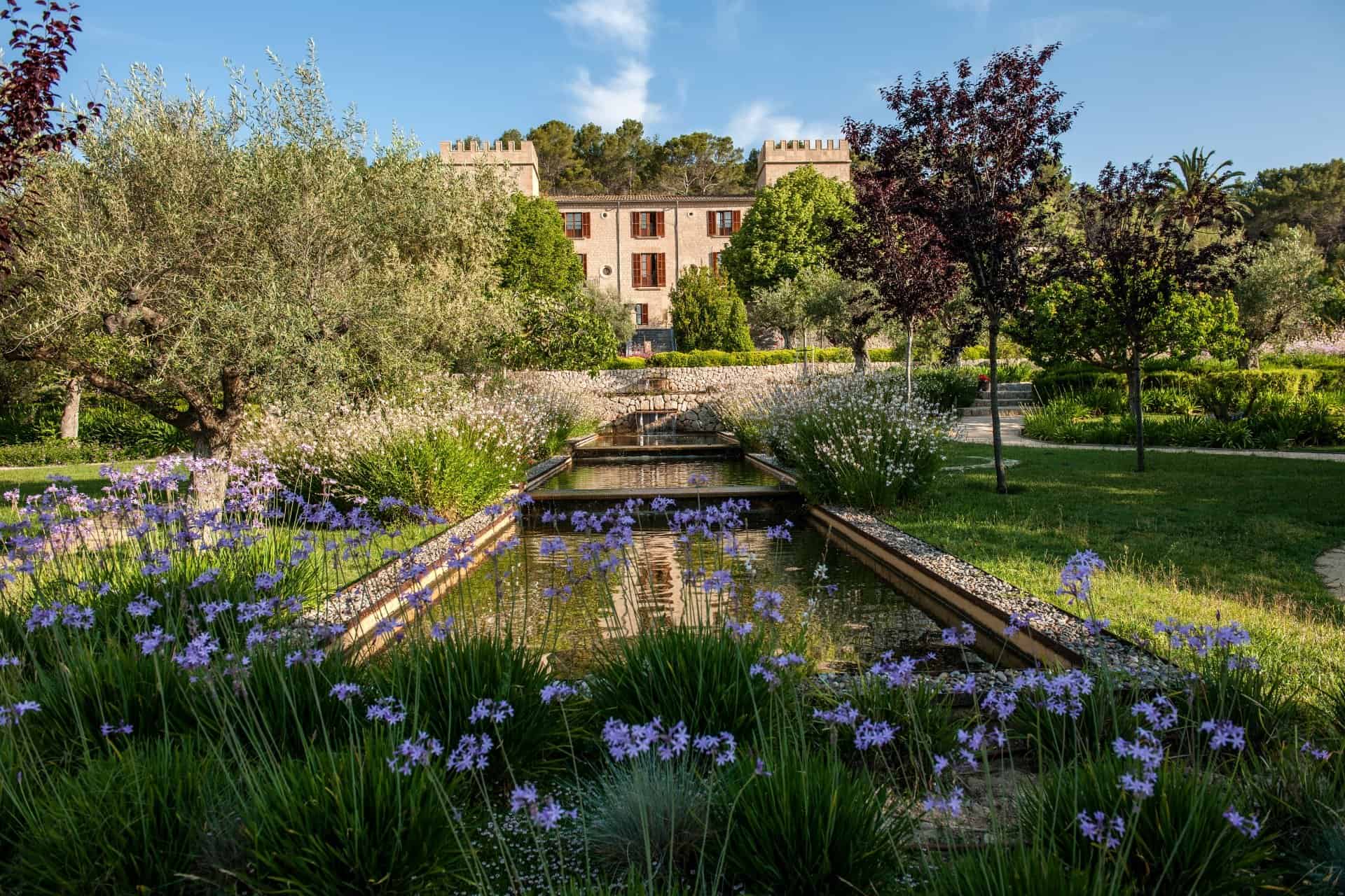 Reflecting pool and purple flowers in the garden at Castell Son Claret, one of the best places for where to stay in Mallorca