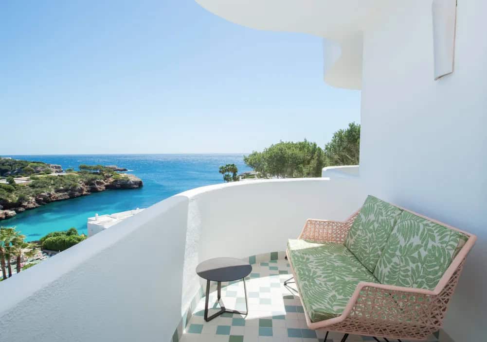 Rattan sofa on a balcony overlooking a turquoise cove, a scenic spot for where to stay in Mallorca