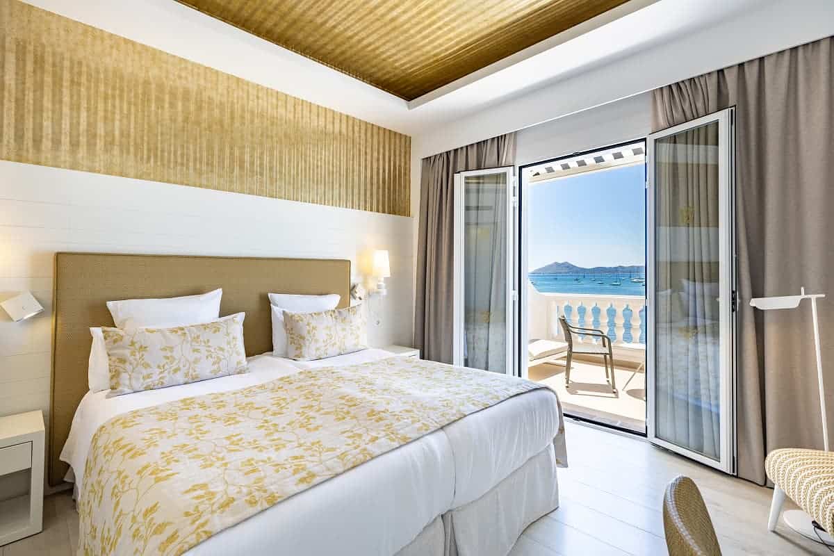 Bedroom with gold accents and a sea view balcony overlooking boats in Puerto Pollensa, Mallorca