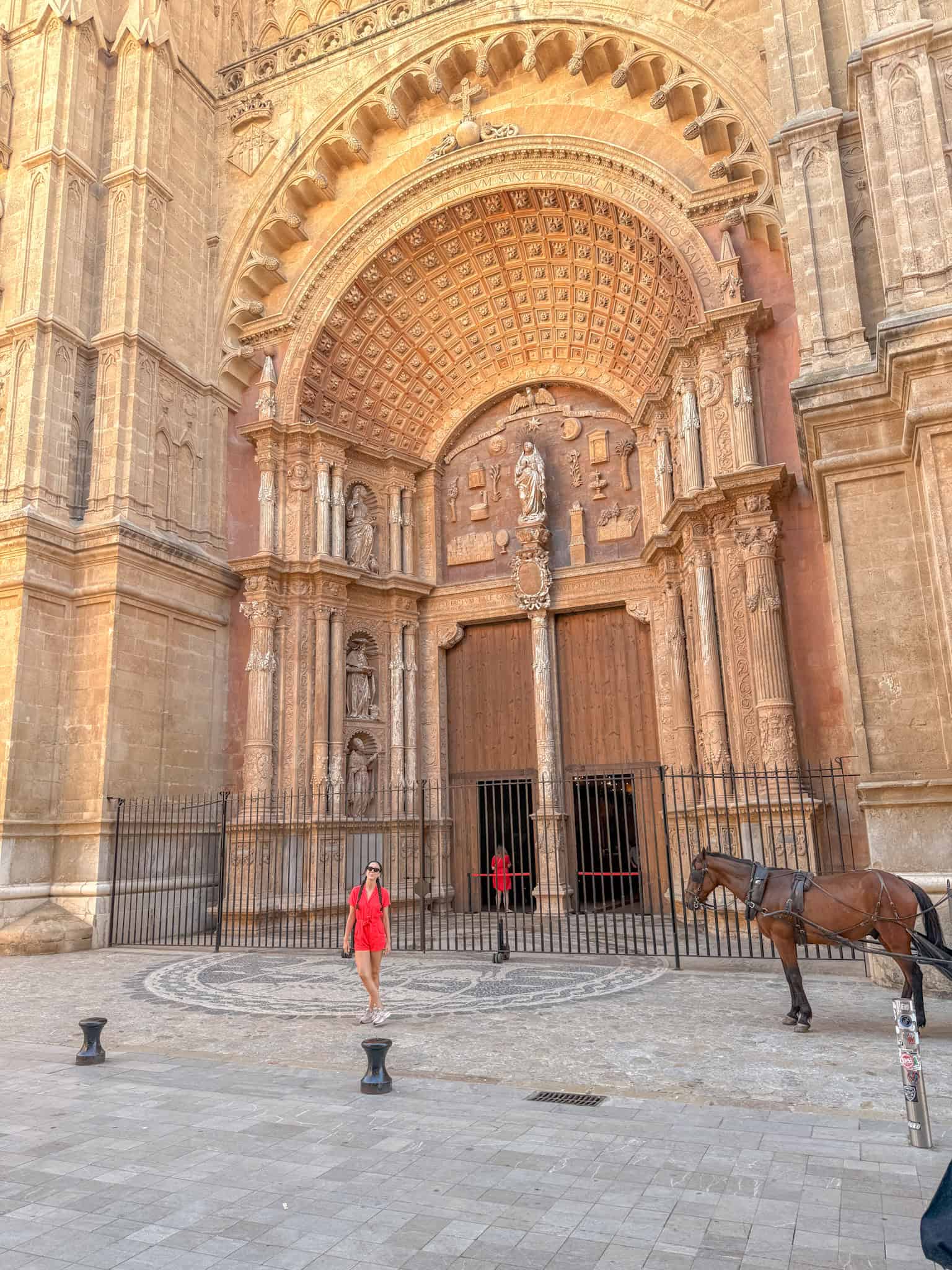 Woman in a red dress outside the ornate main portal of Palma Cathedral, Mallorca